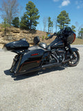 Black touring motorcycle parked on road with saddlebags, trees and rock hillside background