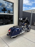 Blue Indian motorcycle parked outside by building and chain-link fence, palm trees reflected in window